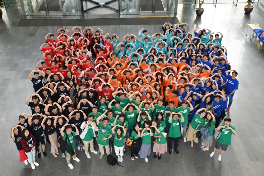 다양한 색의 티셔츠를 입은 임직원 200여명이 팔로 하트를 만들어 보이며 단체 사진을 촬영하고 있다. 